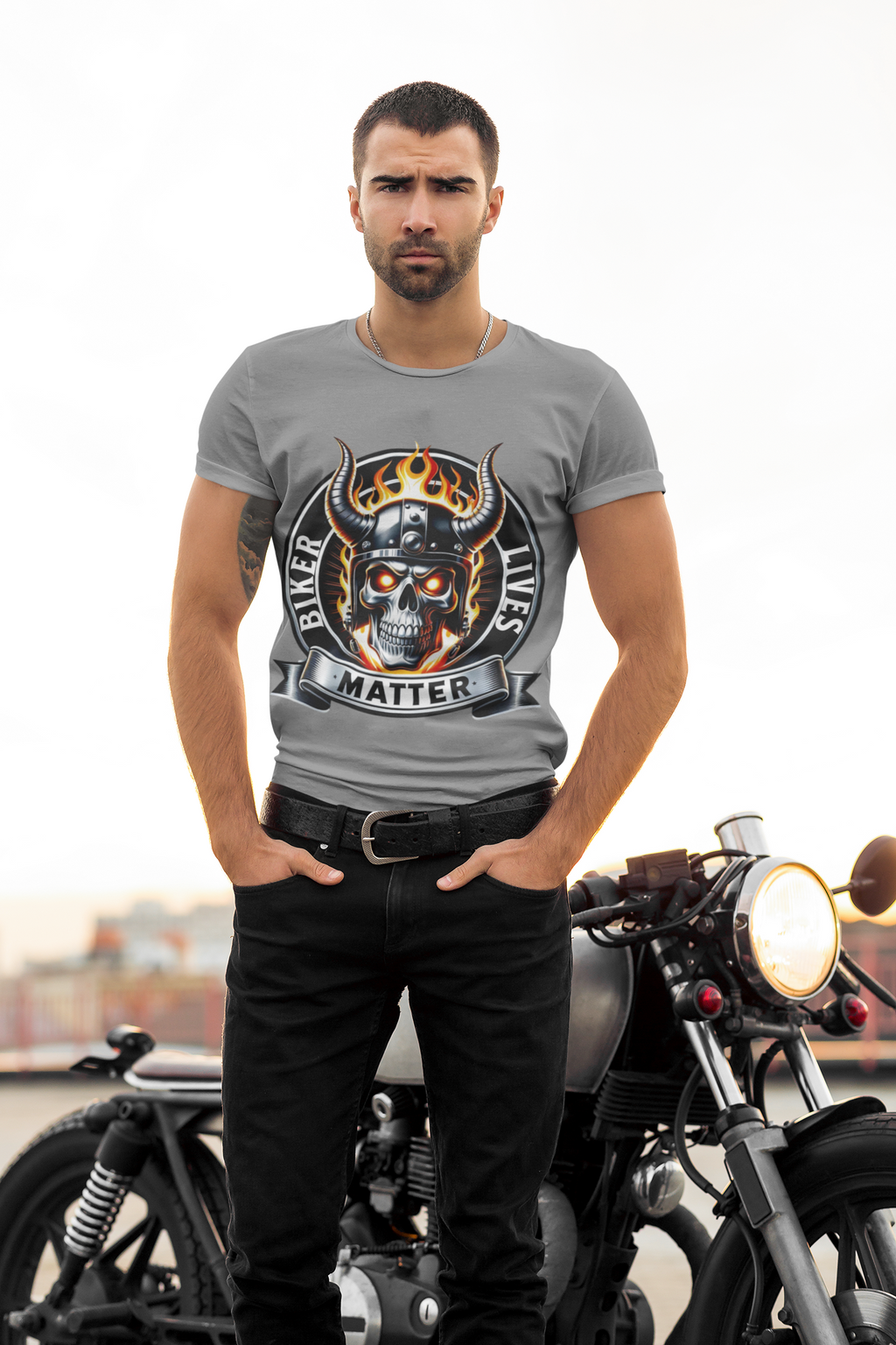 A man wearing a gray t-shirt with a biker skull graphic that reads 'Biker Lives Matter' stands in front of a motorcycle.