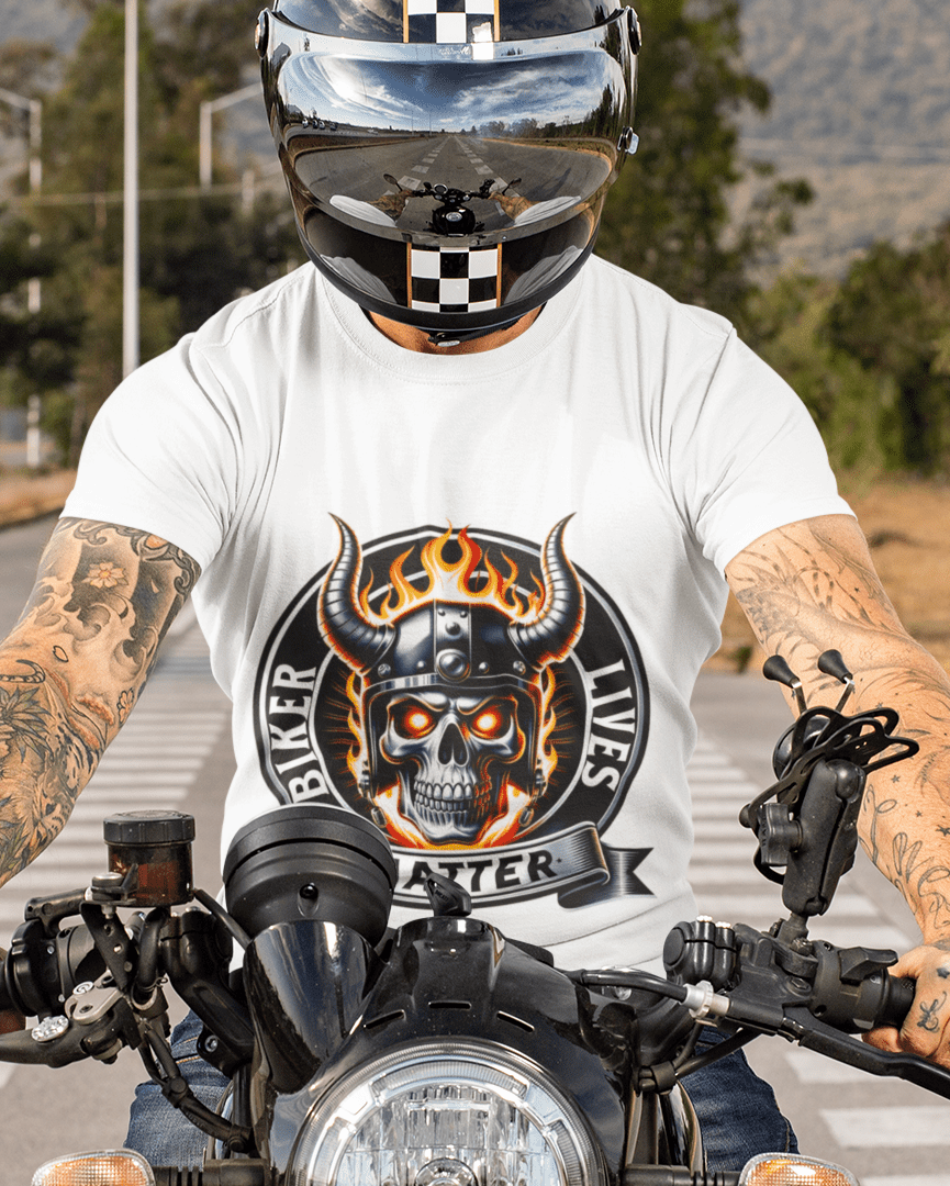 A person wearing a white graphic t-shirt with a skull and flames design, blue jeans, and a black helmet with a checkered visor, riding a motorcycle on a paved road with hills in the background.
